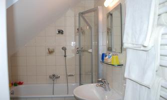 A modern bathroom with a bathtub and a separate shower. The walls are light tiled and provide a clean, welcoming atmosphere.