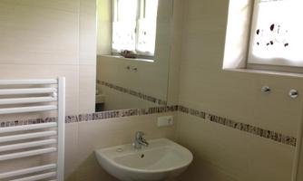 A modern bathroom with a sink and a large mirror. On the wall, there is a towel radiator and a window with white curtains.