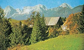 A picturesque landscape with high mountains in the background and a small farm. Surrounded by trees and lush greenery.