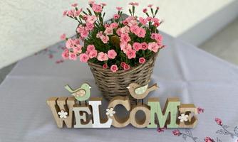A welcome sign made of wood stands next to a basket of pink flowers. The atmosphere is friendly and inviting.