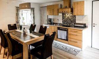 A modern kitchen with wooden cabinets and a large dining table. The kitchen is bright and inviting, ideal for shared meals.