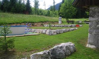 A quiet garden with a lawn area and stones. In the background, there is a above-ground pool and some trees visible.