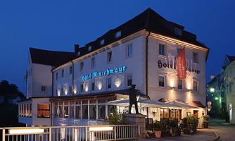 A charming hotel with blue lighting at night. In front of the building, there are outdoor tables and a cozy atmosphere.