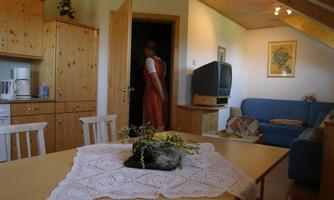 A cozy room with wooden furniture and a large window area. On the table lies a decorative tablecloth and a flower arrangement.