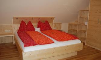 A cozy bedroom with a wooden frame bed. The colorful pillows in red and the wooden shelves give the room an inviting atmosphere.