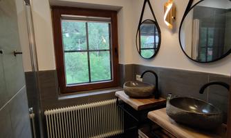 A modern bathroom with two round mirrors and stylish stone sinks. Natural light falls through the window onto the elegant furnishings.