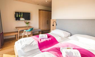 A modern bedroom with two beds and fresh white towels. A table and a television complement the cozy furnishings.