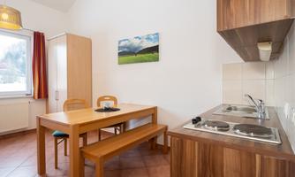 A bright and cozy kitchen with a wooden table and benches. The walls are in soft colors, and a picture of a landscape painting hangs on the wall.