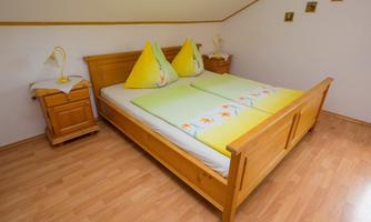 A cozy bedroom with a wooden bed and colorful cushions. Next to the bed is a nightstand with a lamp.