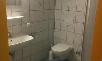 A simple bathroom with white tiles and blue floor tiles. There is a shower, a sink, and a toilet.