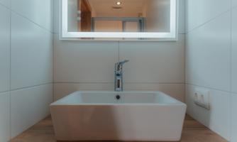 A modern sink on a wooden shelf with a large mirror above it. The walls are simply and brightly designed.