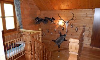 A rustic interior with a wooden staircase and a grid bed. Hunting trophies and antler pieces hang on the wall.