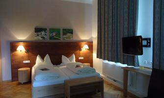 A cozy hotel room with two beds, wooden furniture, and decorative pictures on the wall. The room is well-lit and offers a view of a television and a table.