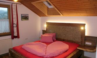A cozy bedroom with a heart-shaped bed and wooden ceiling. The decoration is rustic and inviting.