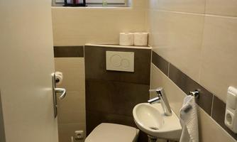 A small bathroom with bright tiles. It contains a toilet, a washbasin, and a window overlooking the outdoors.