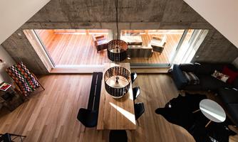 A modern living room with wooden floors and large windows. The space is minimally furnished, with a dining area and a cozy sitting corner.