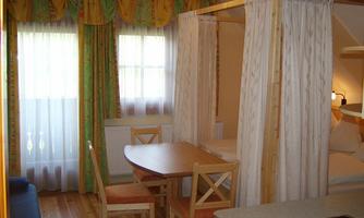 A cozy room with a dining table, chairs, and a bed surrounded by curtains. The ambiance is bright and friendly with colorful drapes.