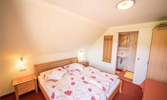 A cozy bedroom with a double bed and a blooming bedspread. To the right is a bathroom with modern amenities.