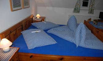 A cozy bedroom with a large bed and blue pillowcases. Soft light from a bedside lamp creates a relaxed atmosphere.
