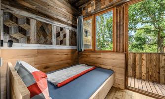 A simple room with wooden walls and a bed. Large windows offer a view of the green surroundings.