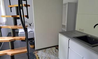 A modern apartment with a wooden staircase and a small kitchen. The space is brightly and friendly furnished.