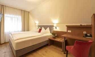 A cozy bedroom with a double bed and wooden floor. A desk and a red chair are also available.