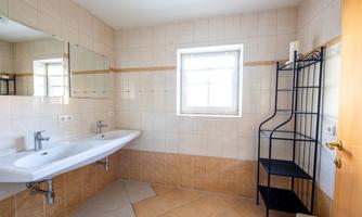 A modern bathroom with two sinks and large mirrors. The space is bright and laid out with ceramic tiles.