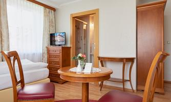 A cozy room with a round table and two chairs. In the background, a bed and a television are visible.