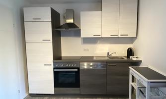 A modern kitchen with bright cabinets and a cooking area. The floor is made of gray wood and there is a small serving cart.
