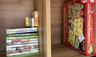 A wooden shelf with a collection of video games and a board game. The games are neatly arranged, while the board game stands prominently beside it.