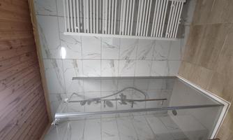 A modern bathroom with a glass shower and bright tiles. On the wall, there is a towel radiator.
