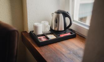 An elegant kettle is sitting on a table next to two cups. On a tray, there are tea bags and sugar.