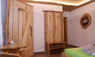 A cozy room with wooden furniture and a bright, modern design. The room features a wardrobe and a wooden seating area.