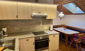 A modern kitchen with wooden paneling and a dining area. The room is well-lit and has a window under the roof.