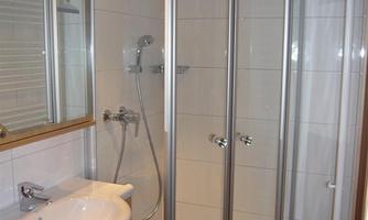 A modern bathroom with a glass shower cabin and bright tiles. On the other side is a sink with wooden details.
