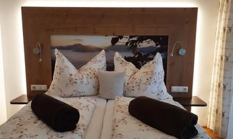 A cozy bedroom with a double bed and decorative pillows. The walls are painted in warm tones, with gentle lighting and a beautiful landscape painting in the background.