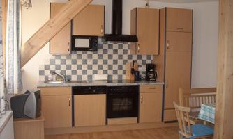 A modern kitchen with wooden cabinets and a tiled backsplash. There is a dining table with chairs and various kitchen appliances.