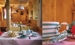 A cozy kitchen with rustic wooden décor and a table set for a meal. On the table are porcelain dishes and a colorful flower as decoration.