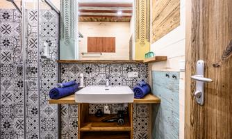 A modern bathroom with stylish tiles and a wooden vanity. The sink is decorated with blue towels, and there is a shower in the corner.