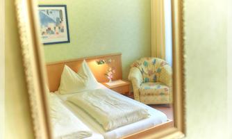 A cozy bedroom with two beds and an armchair. The walls are painted in a soft green and a picture hangs above the bed.
