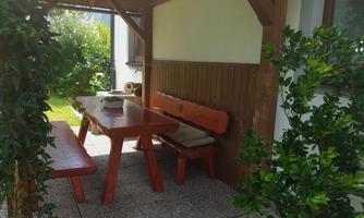 A cozy seating area with a wooden table and benches under a canopy. Surrounded by plants and a well-maintained garden.
