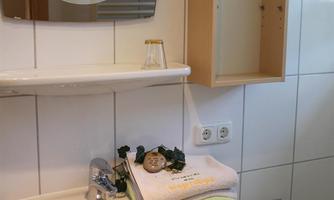 A bright bathroom with a sink and shelves. Fresh towels in various colors are on the sink.
