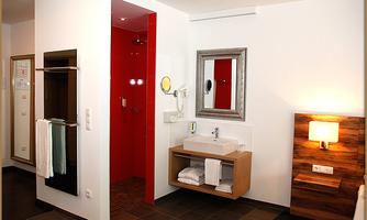 A modern bathroom with a red shower wall and a spacious sink. There are also towels and a wooden cabinet.