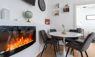 A modern living room with an elegant table and comfortable chairs. On the wall, there is an electric fireplace that creates a cozy atmosphere.