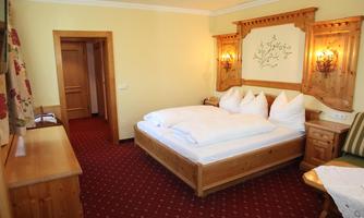 A cozy bedroom with a double bed and large pillows. The warm wood details and the red carpet design give the room an inviting atmosphere.