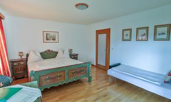 A cozy bedroom with a large bed and an additional sofa bed. The walls are bright and there are some pictures for decoration.