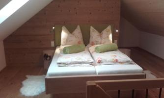 A cozy attic room with a double bed and nice cushions. The wooden floor and walls give the room a warm atmosphere.