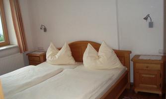 A simple bedroom with a large double bed and two pillows. There are wooden wardrobes and a carpet on the floor.