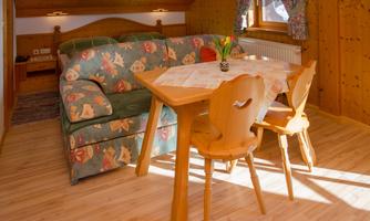 A cozy living area with a sofa and a wooden table. The room has paneled wood walls and plenty of natural light.