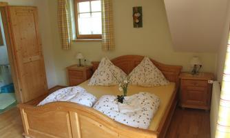 A cozy bedroom with a large wooden bed and two pillows. Next to the bed are nightstands with lamps, and the room has a bright, friendly atmosphere.